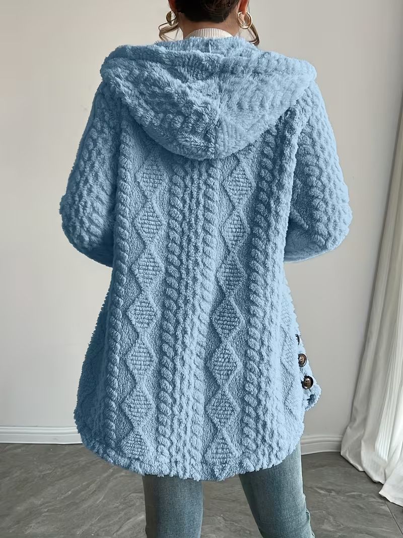 A person viewed from the back wearing a light blue textured hooded cardigan with diamond cable knit patterns and side buttons, paired with gray jeans in an indoor setting.