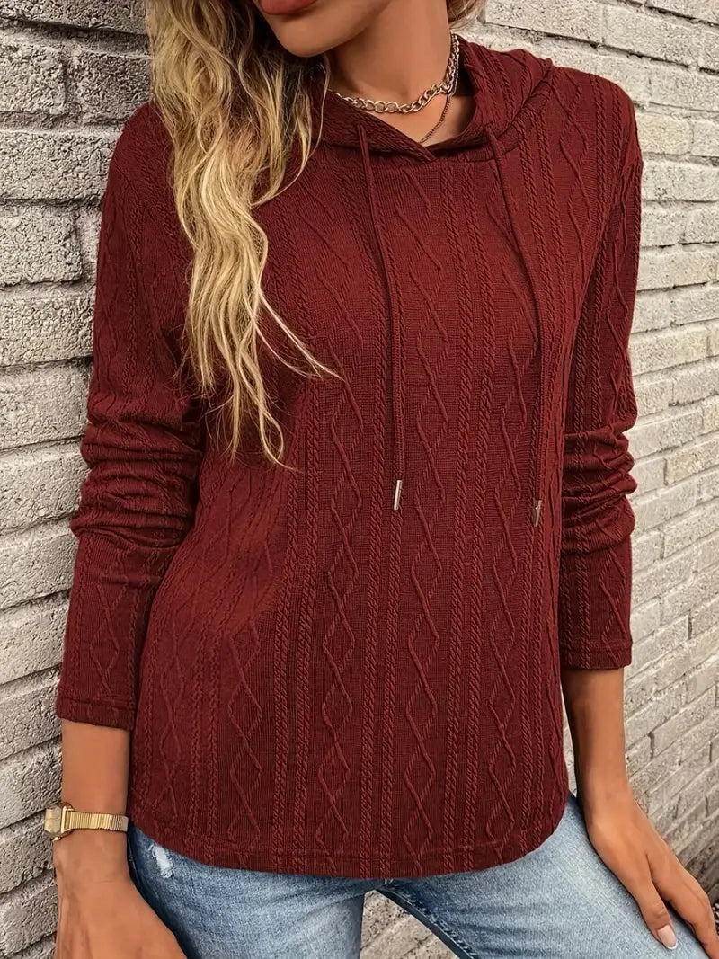 Adeline cable knit hooded pullover, front view against brick wall