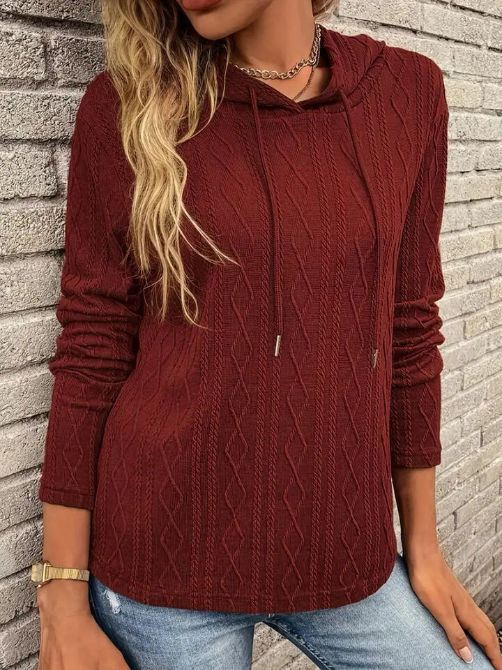 Adeline cable knit hooded pullover, front view against brick wall
