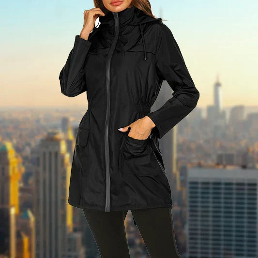 Harper hooded rain jacket in black, front view with hand on hood, city skyline background