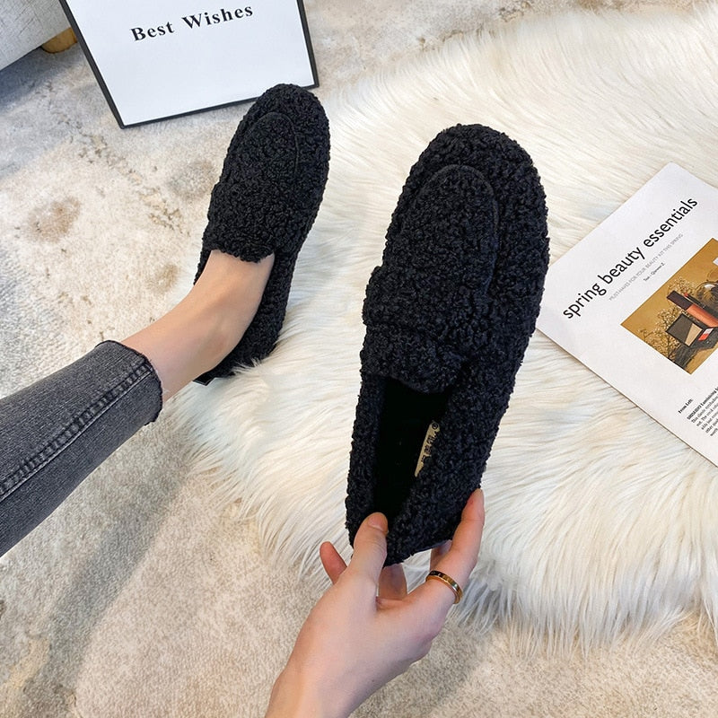 Wren plush slippers in black, held by hand on faux fur rug