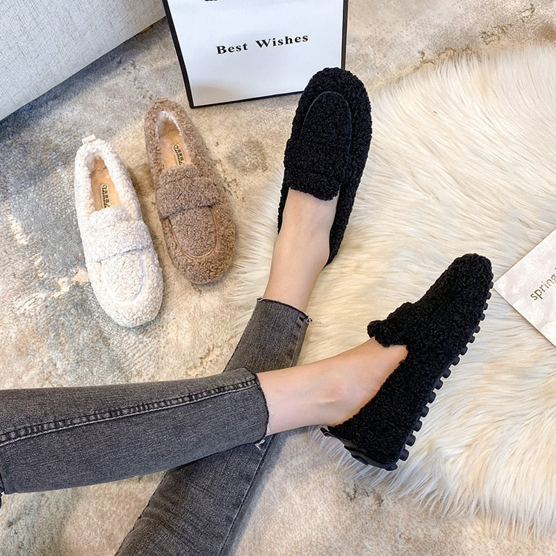 Wren plush slippers in black, held by hand on faux fur rug