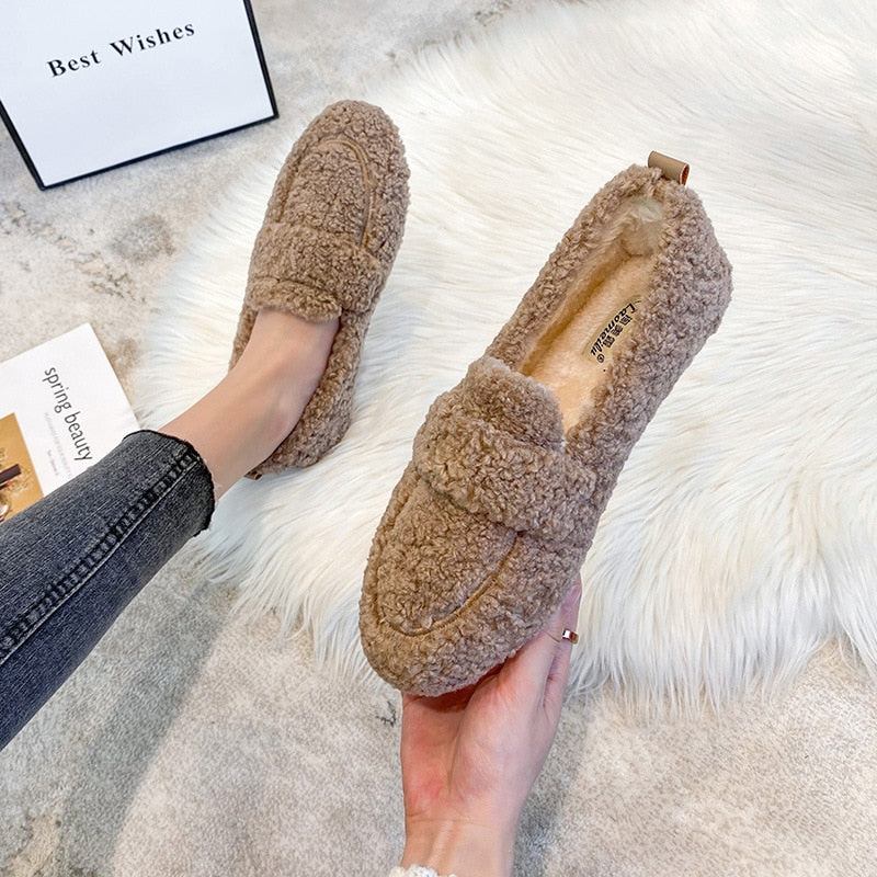 Wren plush slippers in black, held by hand on faux fur rug