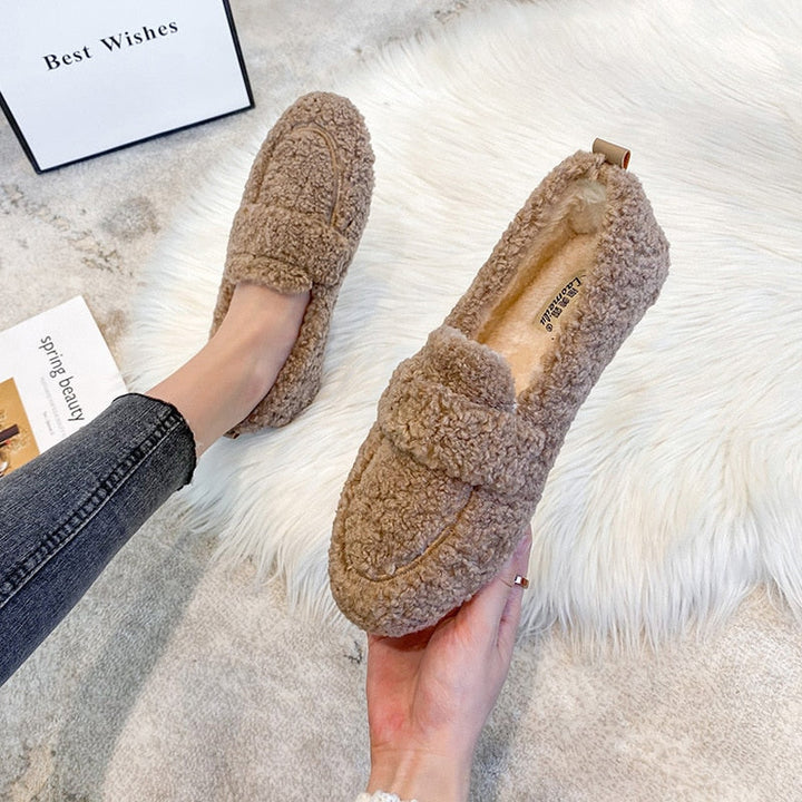 Wren plush slippers in black, held by hand on faux fur rug