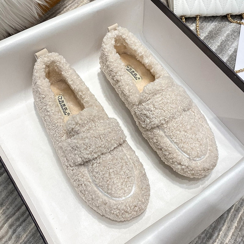 Wren plush slippers in black, held by hand on faux fur rug
