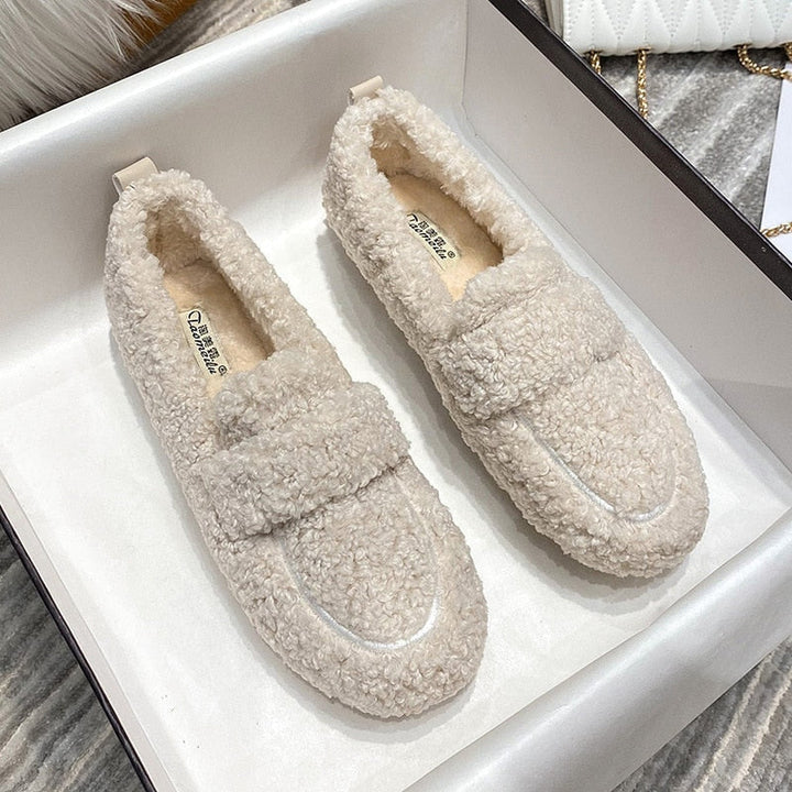 Wren plush slippers in black, held by hand on faux fur rug