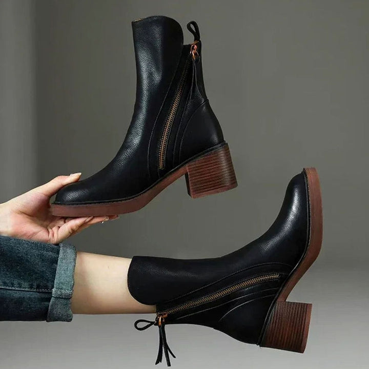 Priscilla black zip-up block heel ankle boots held by hand, side view